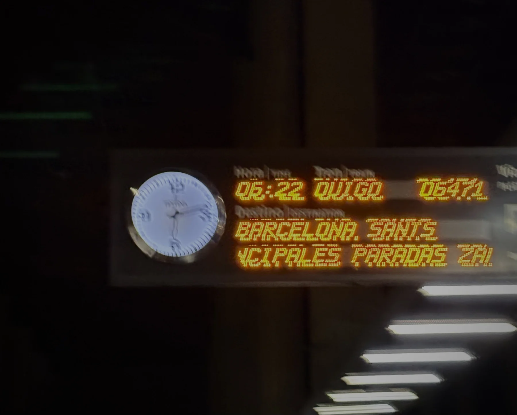 A departures board and station clock glowing in the dark, reading 06:22 to Barcelona Sants.