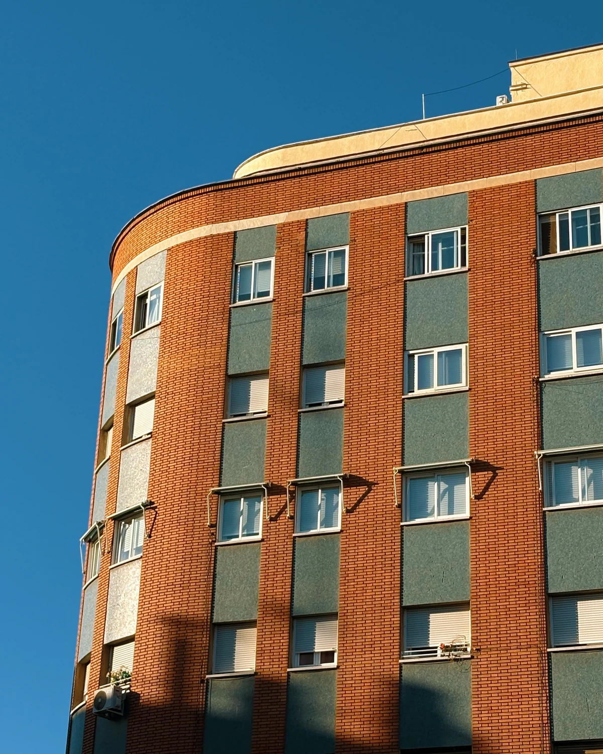 Reddish-brown brick facade with sage-green paneled stripes on a curved building corner
