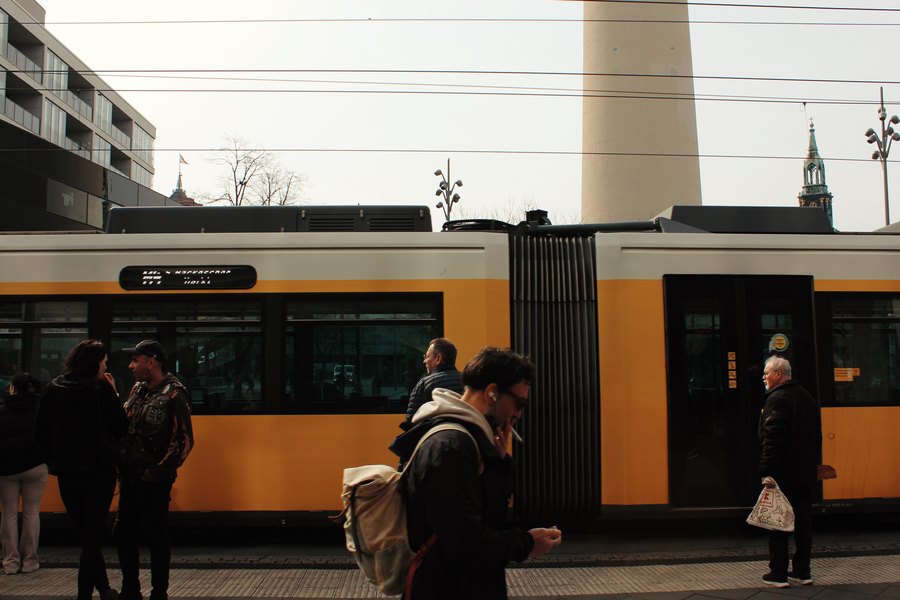 Passengers beside a yellow tram below the Fernsehturm, Berlin
