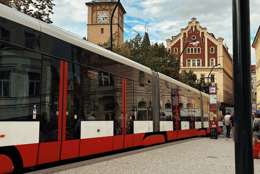 A red Prague tram passing beneath the Karlovy Lazne clock tower