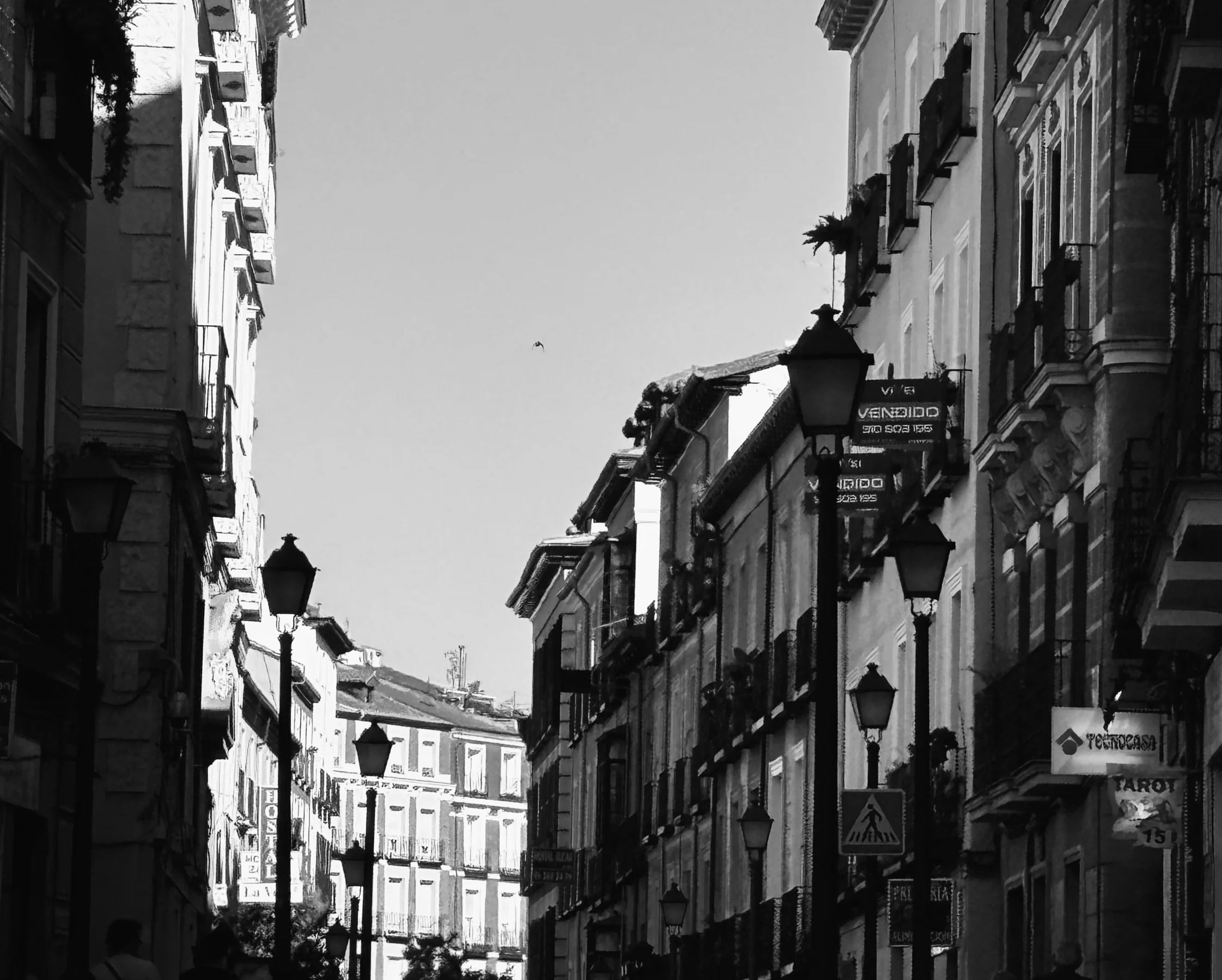 A narrow alley receding to a vanishing point, lamps on both sides, black and white, Madrid