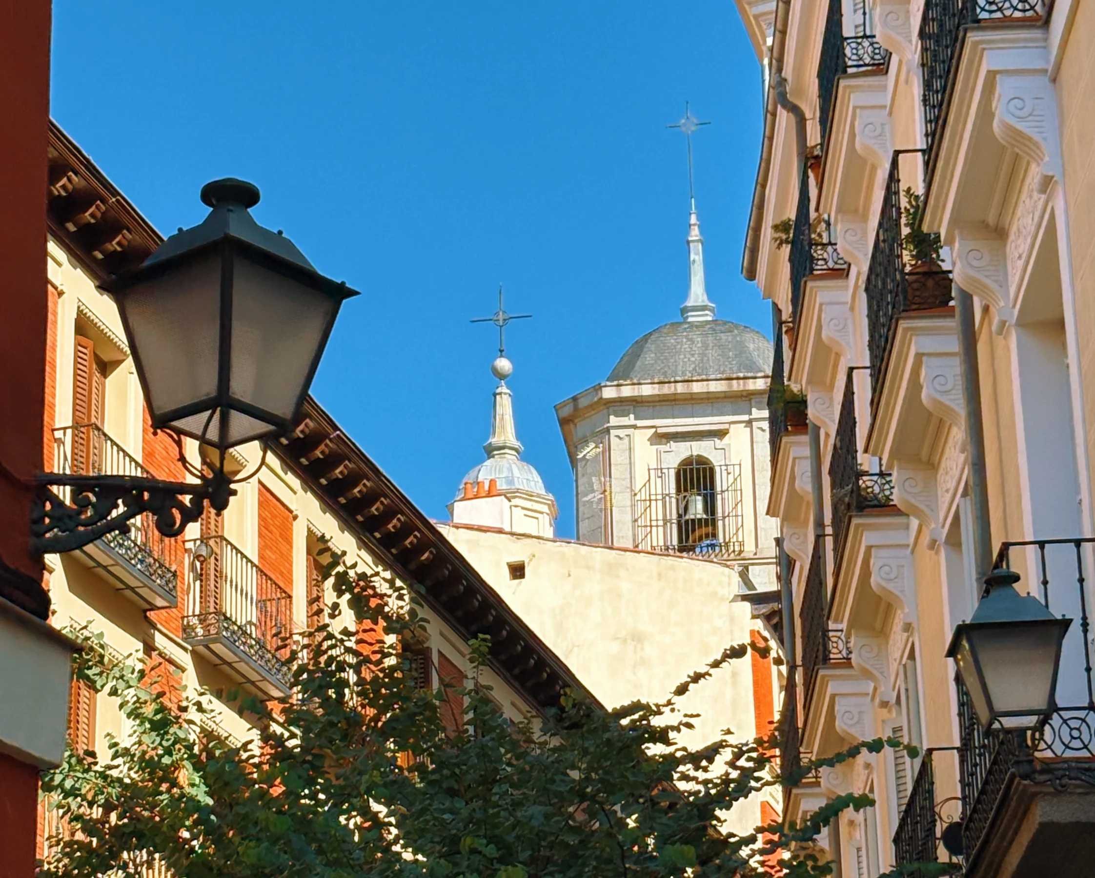 A street lamp beside a domed church spire against a blue sky, Madrid