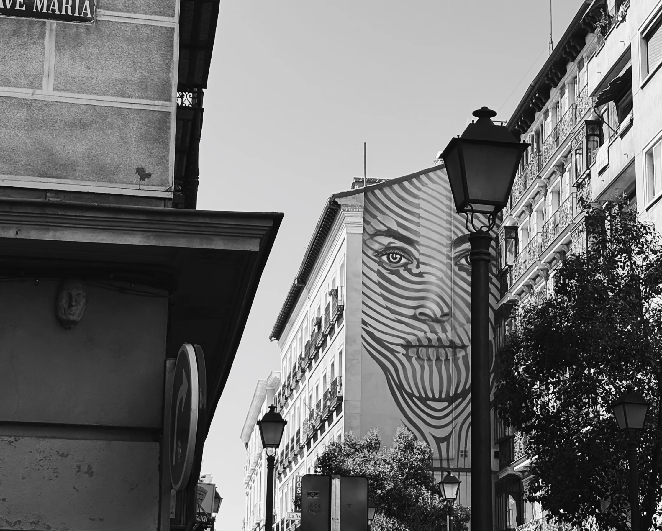 A painted face mural above a street lamp, black and white, Madrid