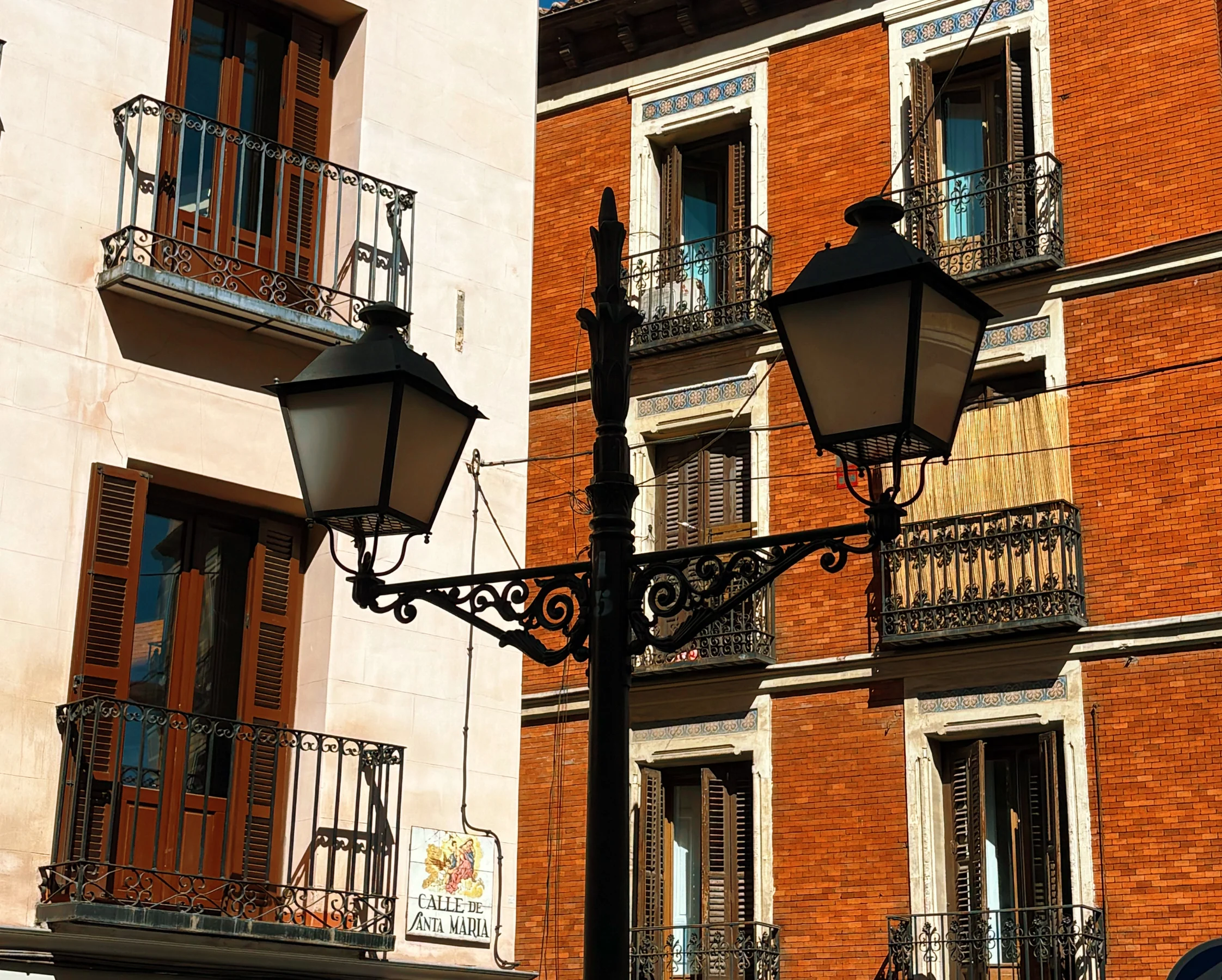 A double lamp post against a red brick building, Calle de Santa Maria, Madrid